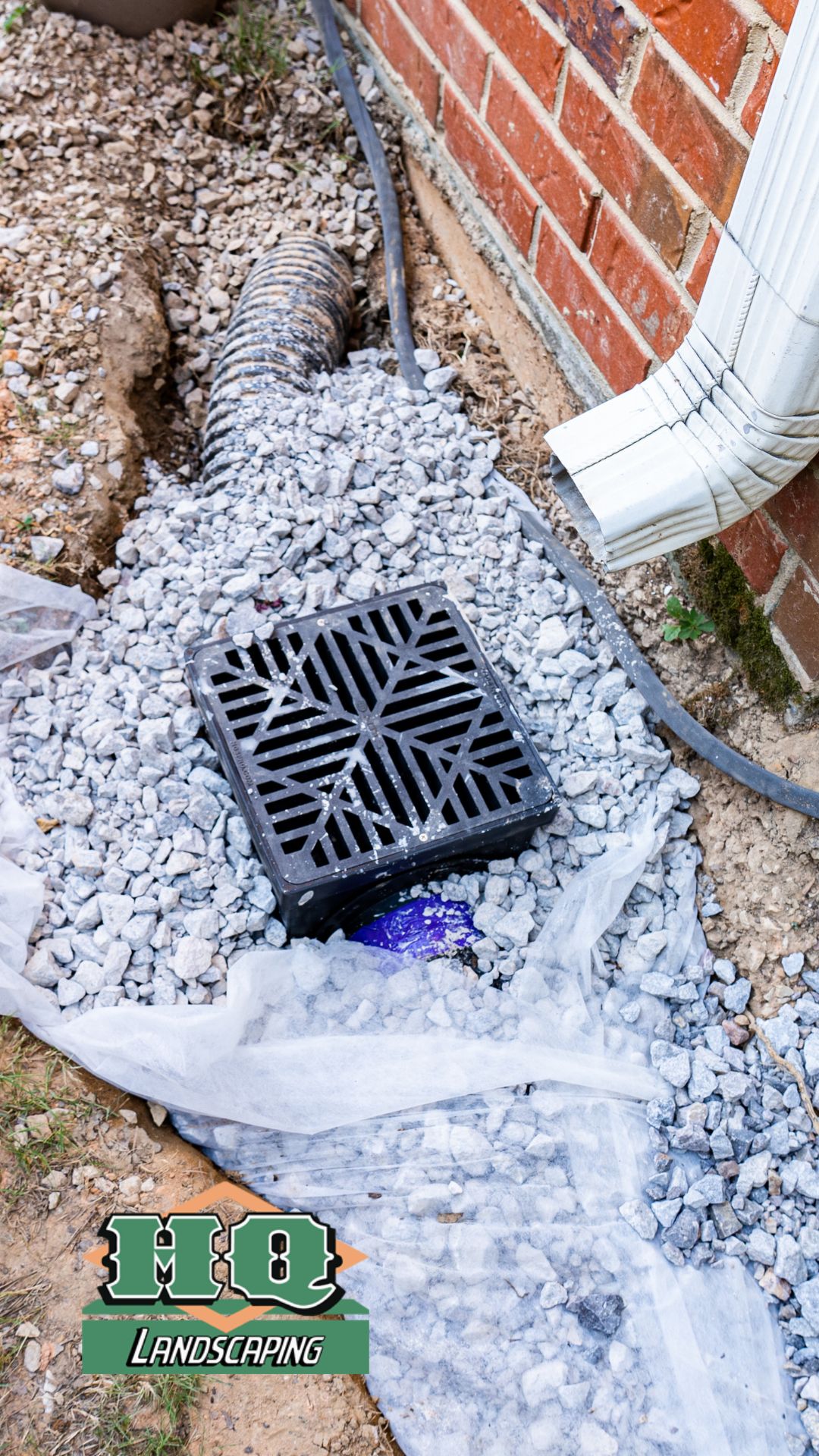 A professionally installed drainage system with a black catch basin, gravel, and a connected downspout, showcasing HQ Landscaping's expert drainage solutions to prevent water damage.